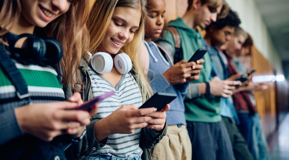 Mehrere Schülerinnen und Schüler stehen auf dem Schulflur und schauen auf ihr Handy.