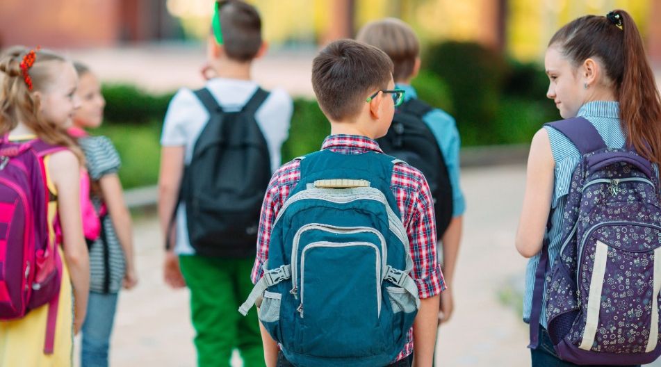 Eine Gruppe von Schulkindern mit Rucksäcken geht gemeinsam draußen, einige schauen sich an und unterhalten sich.Eine Gruppe von Schulkindern mit Rucksäcken geht gemeinsam draußen, einige schauen sich an und unterhalten sich.