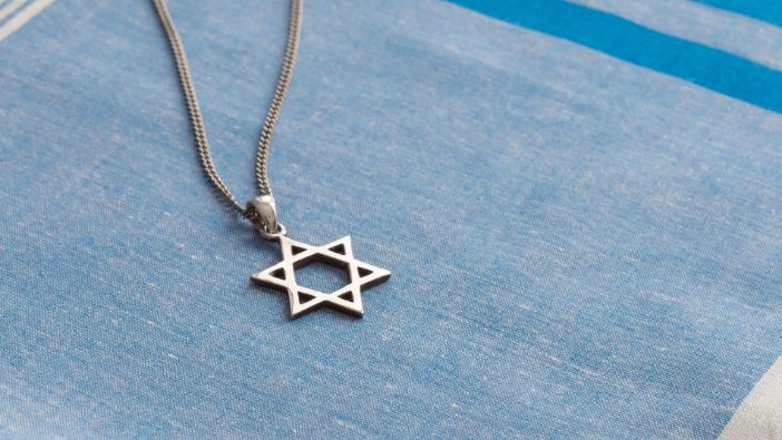 Eine silberne Halskette mit einem Davidstern-Anhänger liegt auf einem blau-weiß gestreiften Stoff.