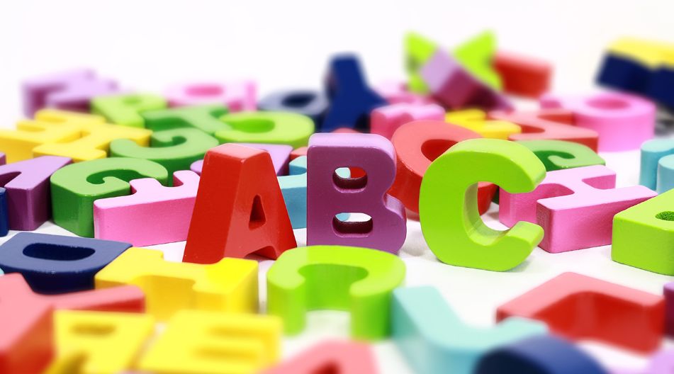 Bunte, plastische Buchstaben und Zahlen liegen verstreut auf einer weißen Oberfläche, mit den Buchstaben "A", "B" und "C" im Fokus.