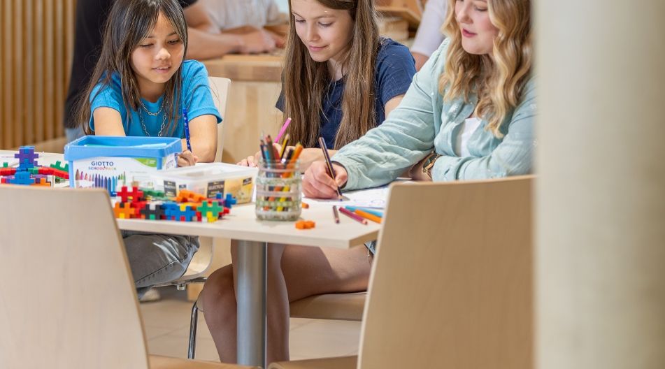 Kinder sitzen in einer Kita an einem Tisch und malen zusammen in einem kreativ gestalteten Raum.