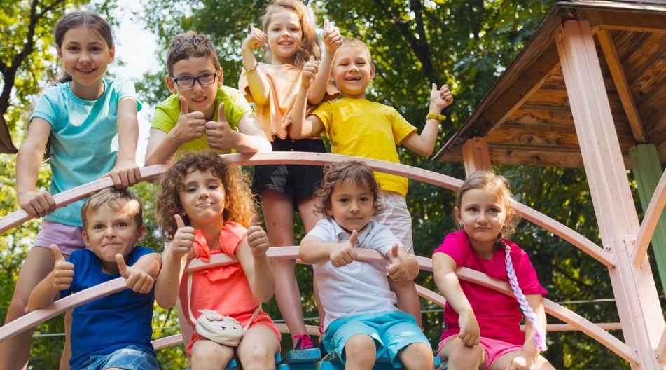 Eine Gruppe fröhlicher Kinder zeigt Daumen hoch auf einem Klettergerüst im Freien.