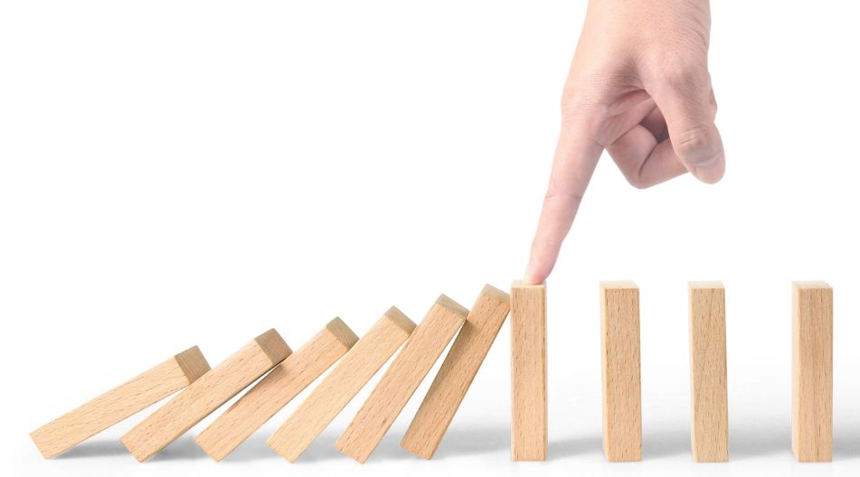 Ein Finger hält eine Reihe von Dominobausteinen in der Mitte auf, sodass die hinteren nicht mehr umfallen können. Ein Finger hält eine Reihe von Dominobausteinen in der Mitte auf, sodass die hinteren nicht mehr umfallen können.