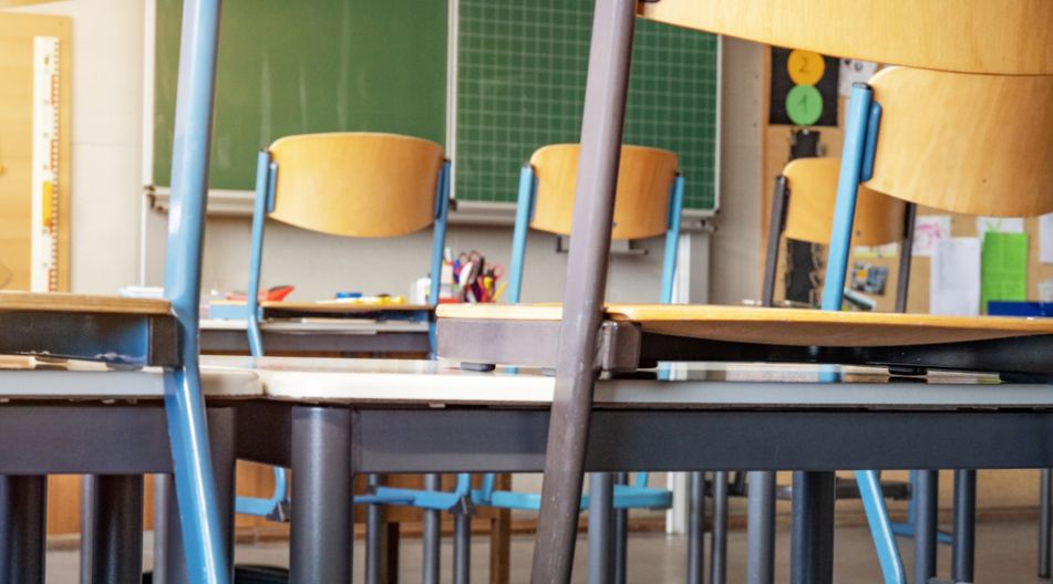 Ein leeres Klassenzimmer mit hochgestellten Stühlen auf den Tischen vor einer grünen Tafel. Ein leeres Klassenzimmer mit hochgestellten Stühlen auf den Tischen vor einer grünen Tafel.